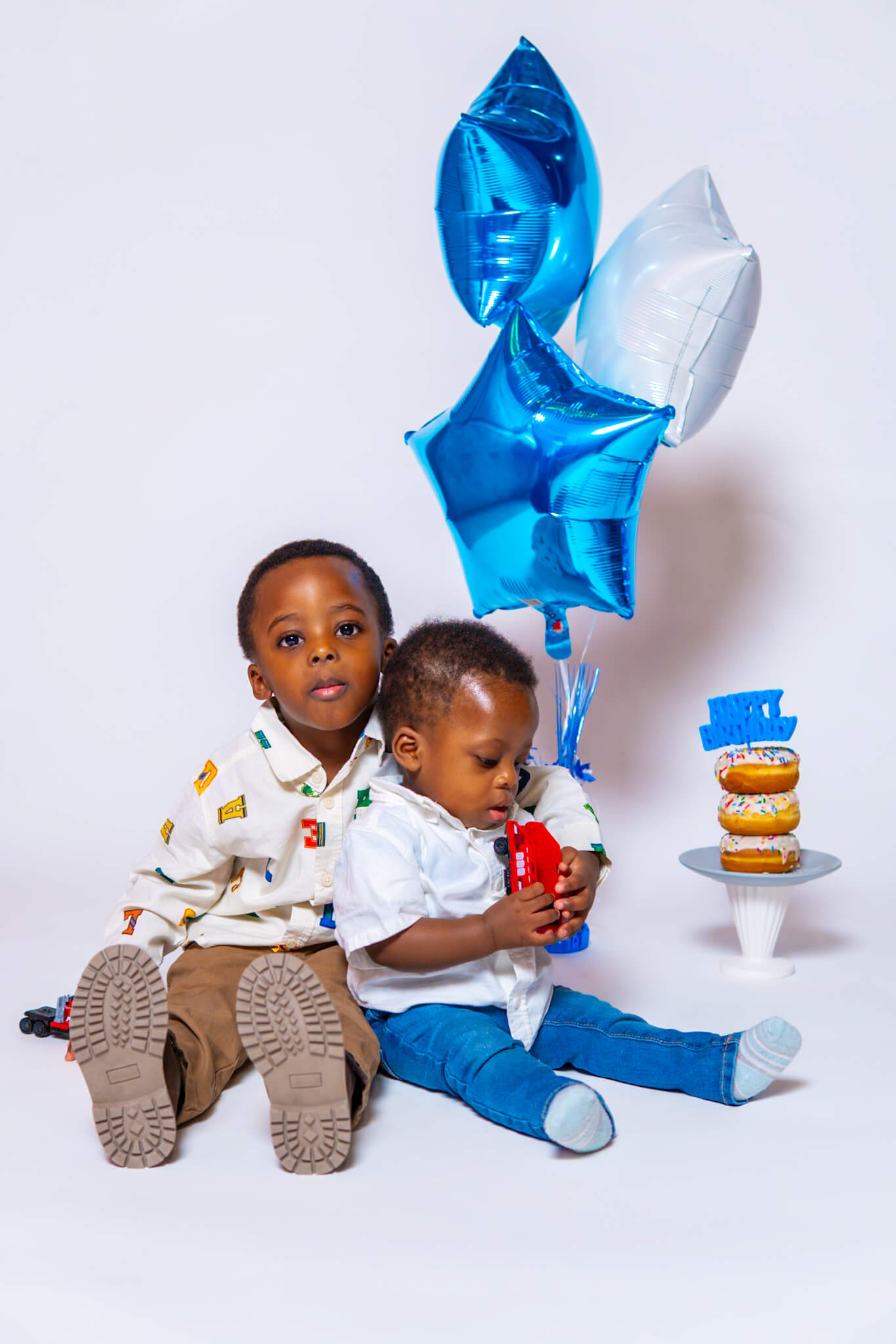 Toddler boy looking at a stack of birthday donuts with blue balloons