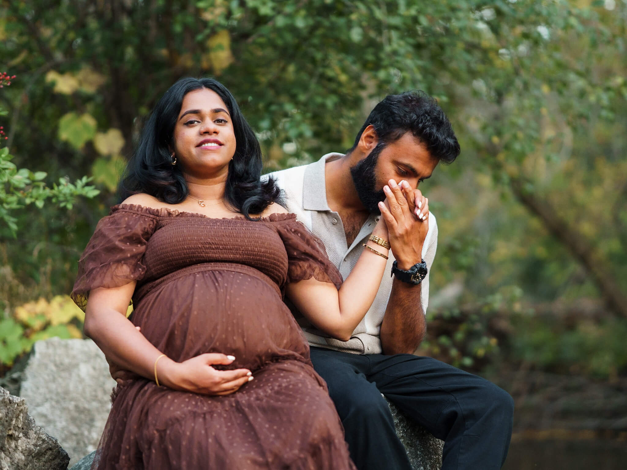 Expectant couple sitting in a wooded area for a maternity session