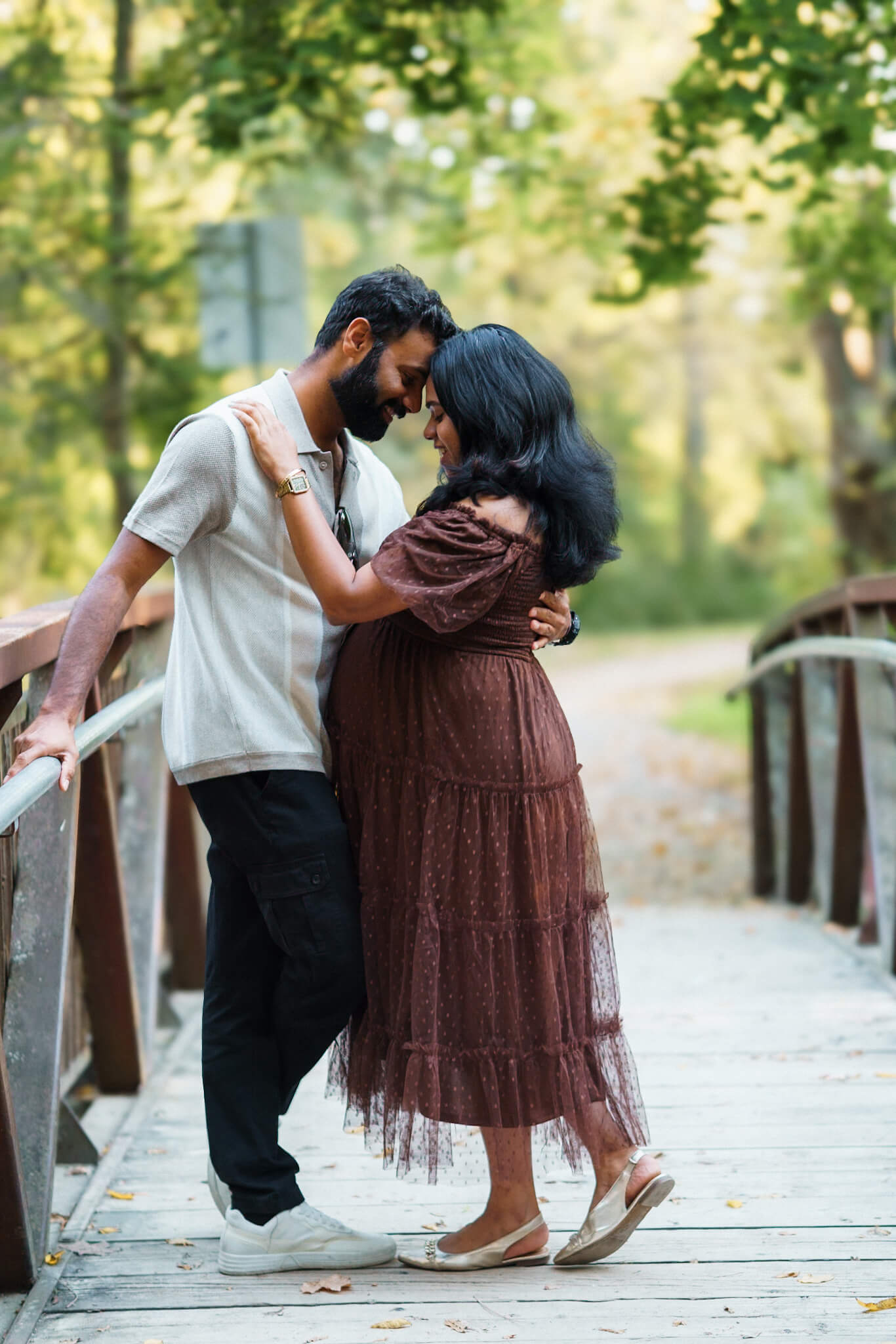 Expectant couple embracing on a wooden bridge in Kitchener
