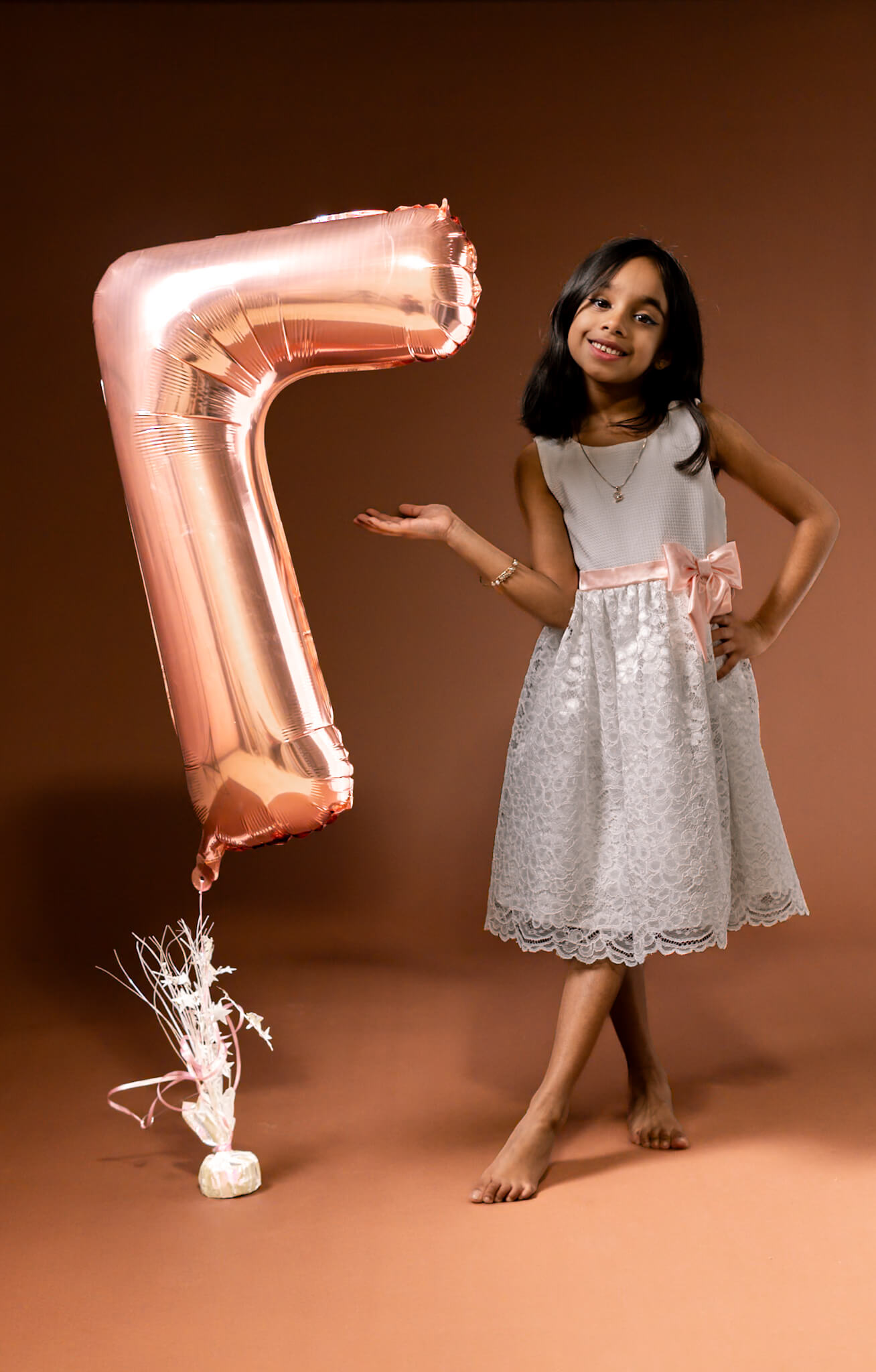 A smiling seven-year-old girl holding festive birthday props in a photo studio